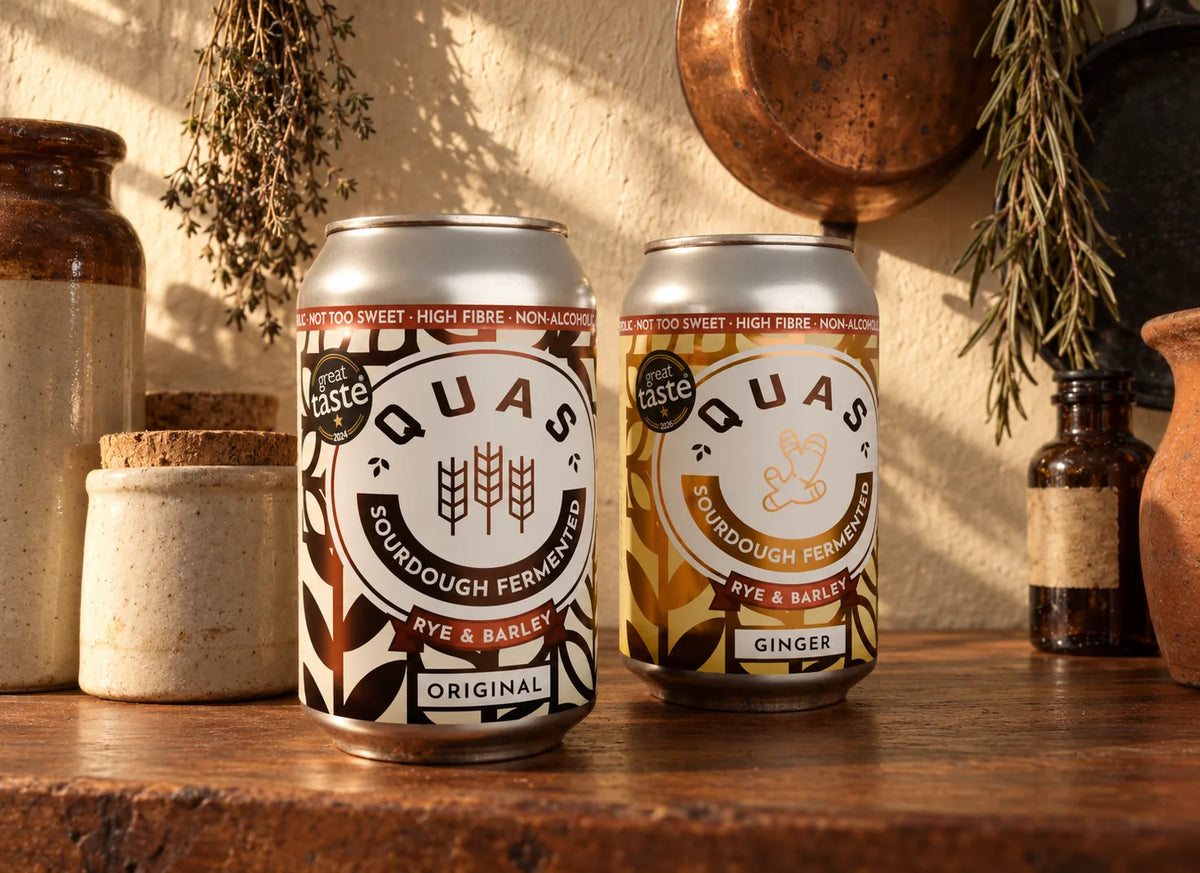 Original and Ginger Quas cans on a kitchen shelf beside stoneware jars and hanging herbs